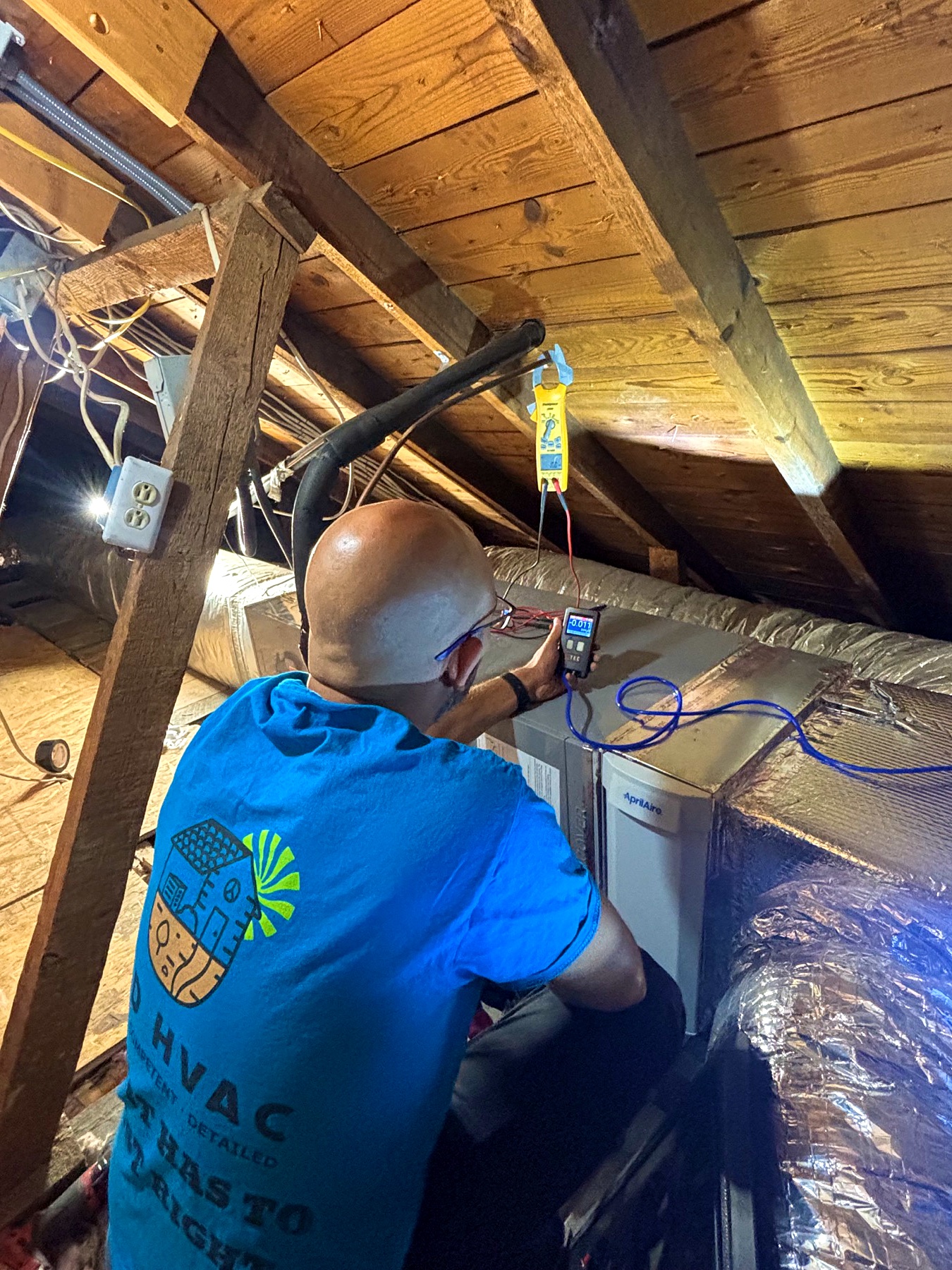 Jacob Myers measuring static pressure and electrical performance in an attic HVAC system.