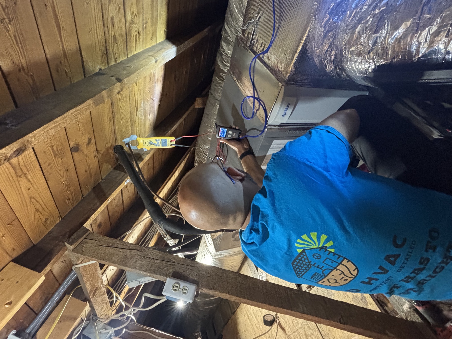 Jacob Myers measuring static pressure and electrical performance in an attic HVAC system.